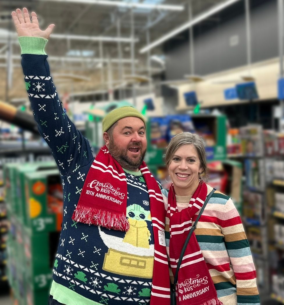 A man and a woman are posing for a picture in a store . the man is wearing a christmas sweater.