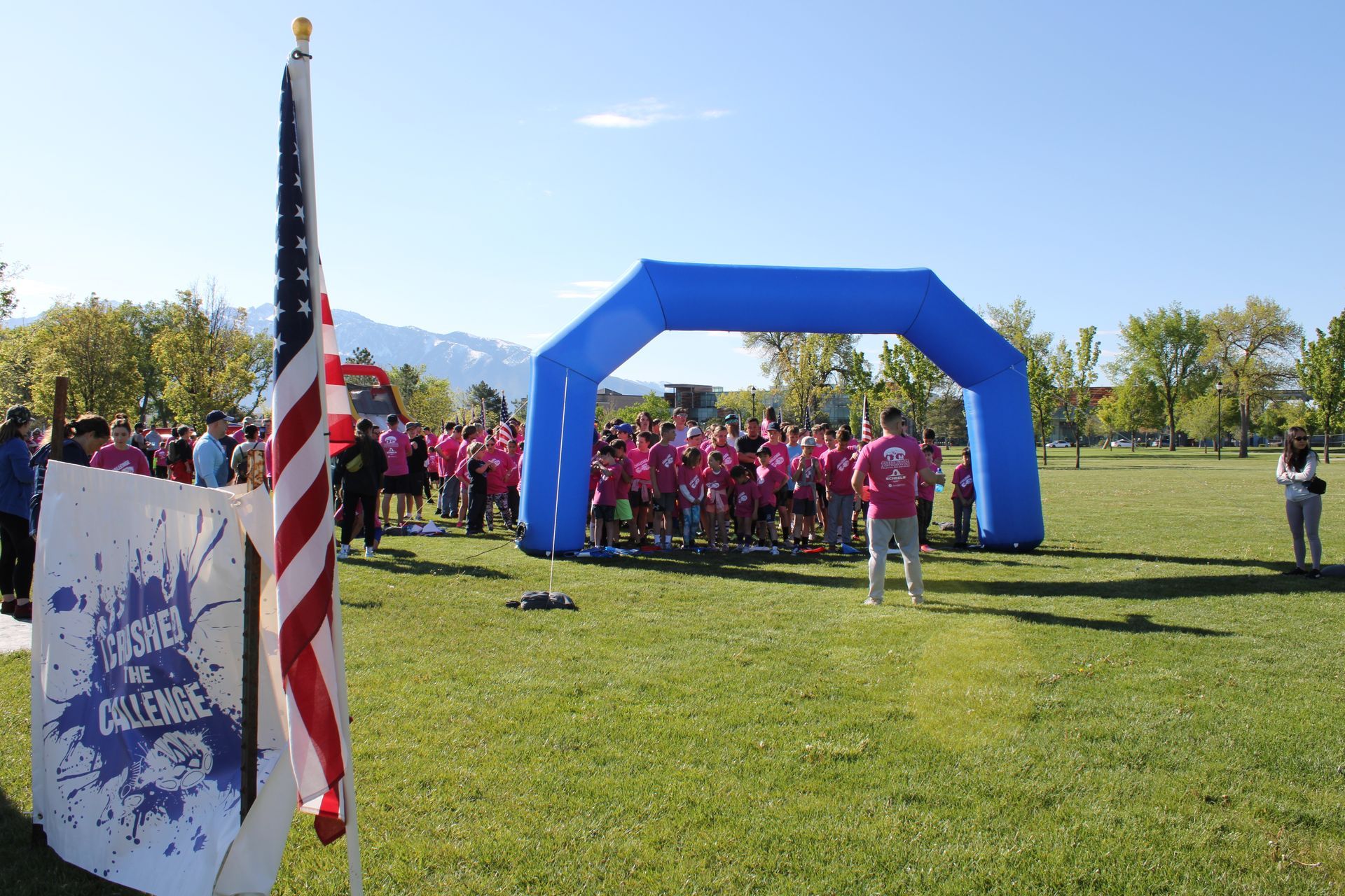 A group of people are gathered in a grassy field in front of an inflatable archway.