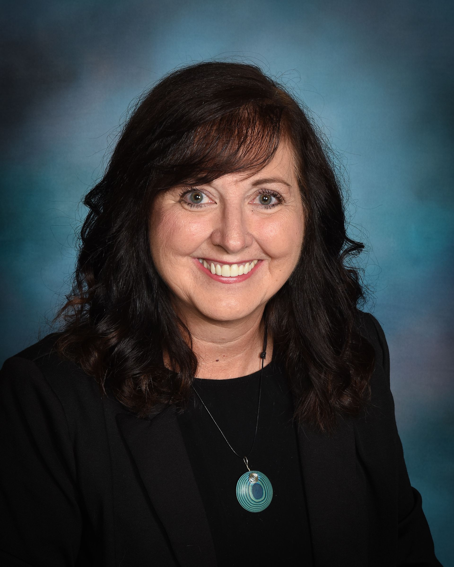 A woman in a black jacket and necklace is smiling for the camera.
