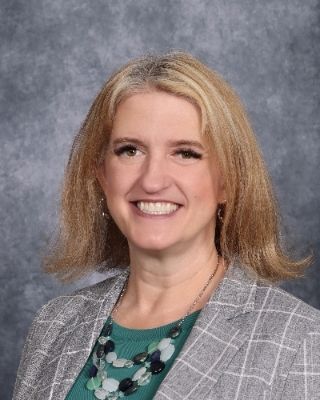 A woman in a pink shirt and black jacket is smiling for the camera.