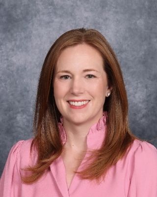 The woman is wearing a pink sweater and smiling for the camera.