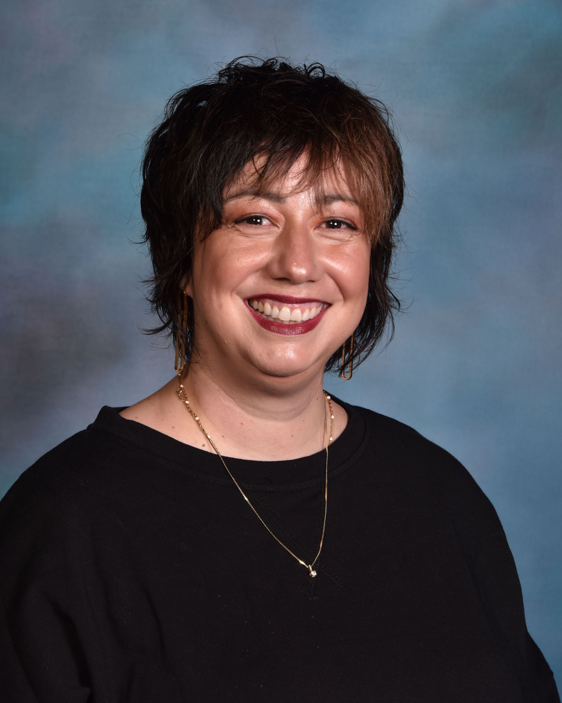 A woman wearing a black shirt and a gold necklace is smiling for the camera.