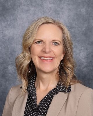 A woman in a blue shirt and black sweater is smiling for a picture.