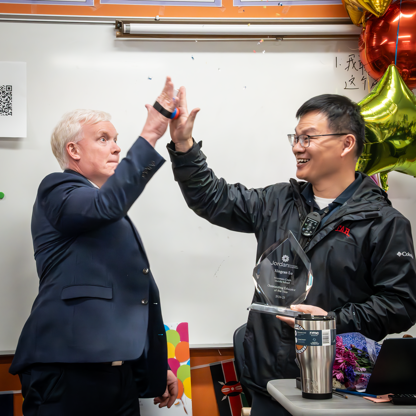 Two men are giving each other a high five in a classroom.