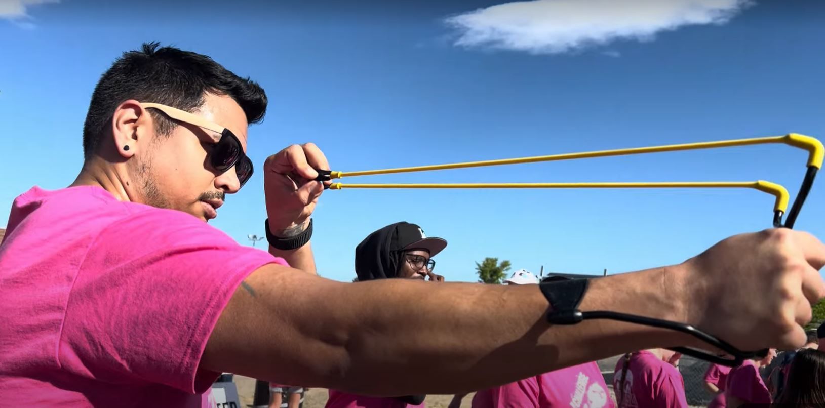 A man in a pink shirt is holding a slingshot in his hand.