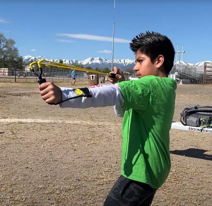 A young boy in a green shirt is holding a slingshot