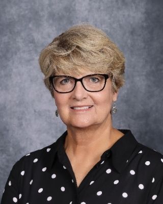 A woman wearing glasses and a green jacket is smiling for the camera.