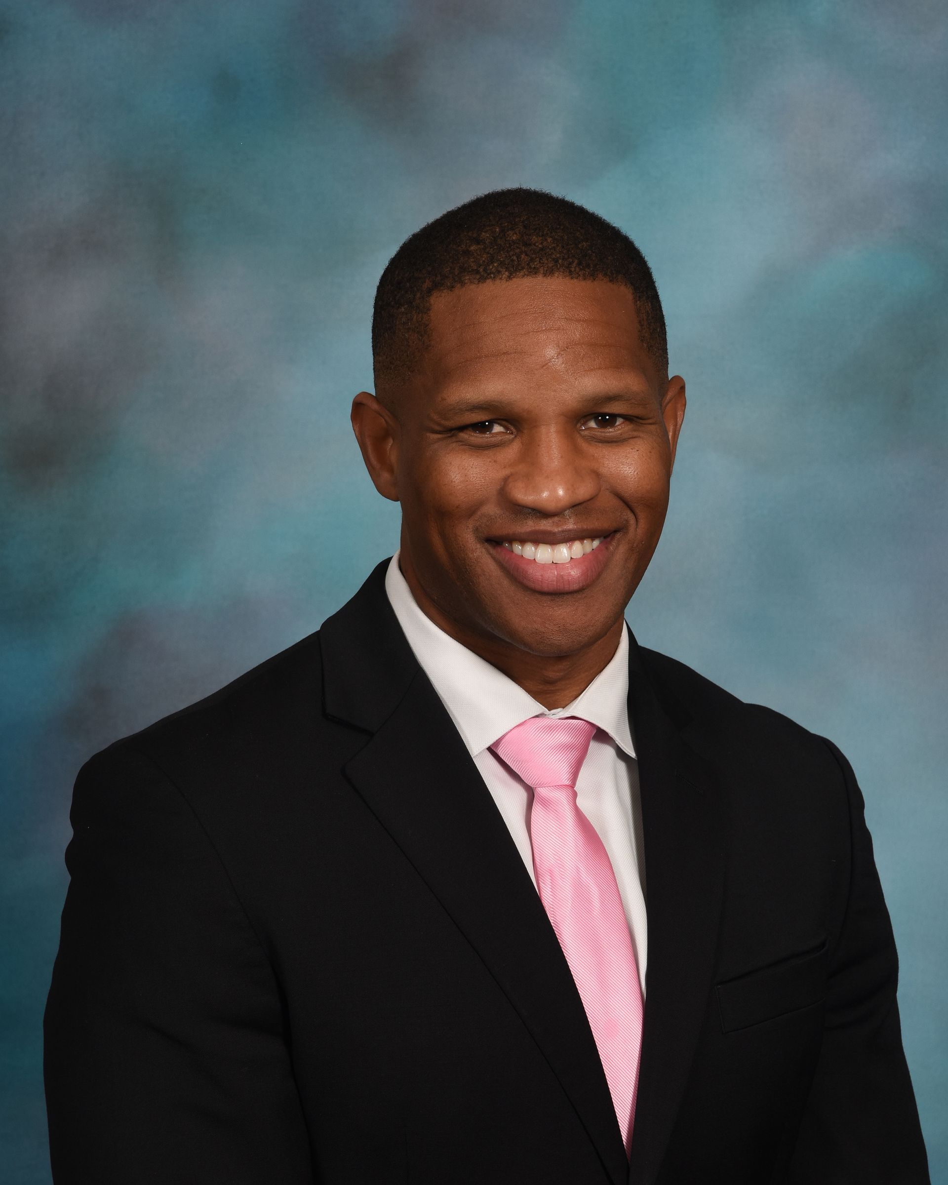 A man in a suit and pink tie is smiling for the camera.