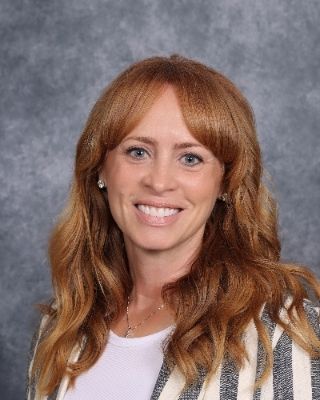 A woman with red hair is smiling for a picture in front of a blue background.