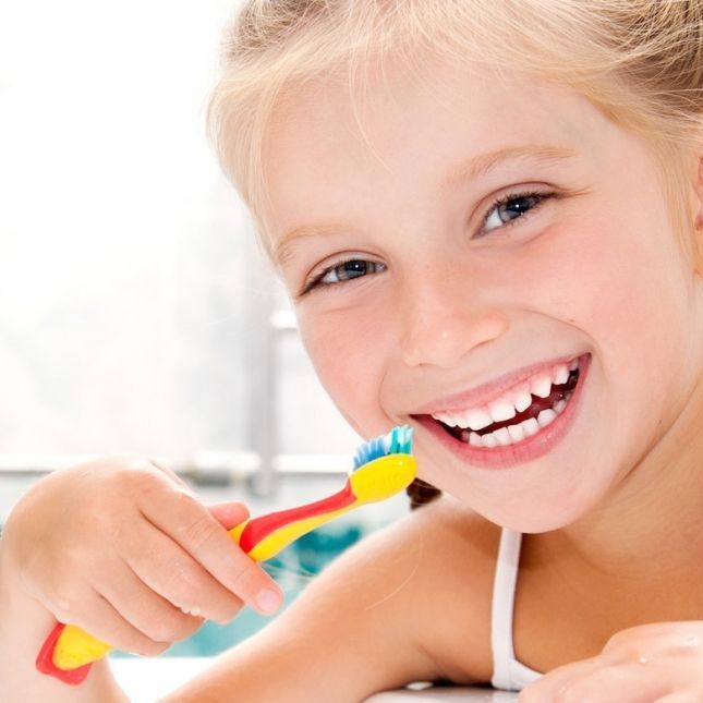 A little girl is brushing her teeth and smiling