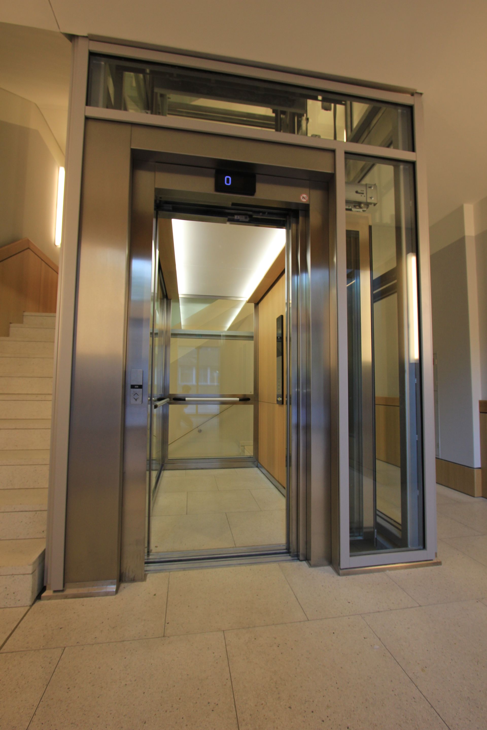 Ein Aufzug mit einer Glastür und einer Treppe dahinter