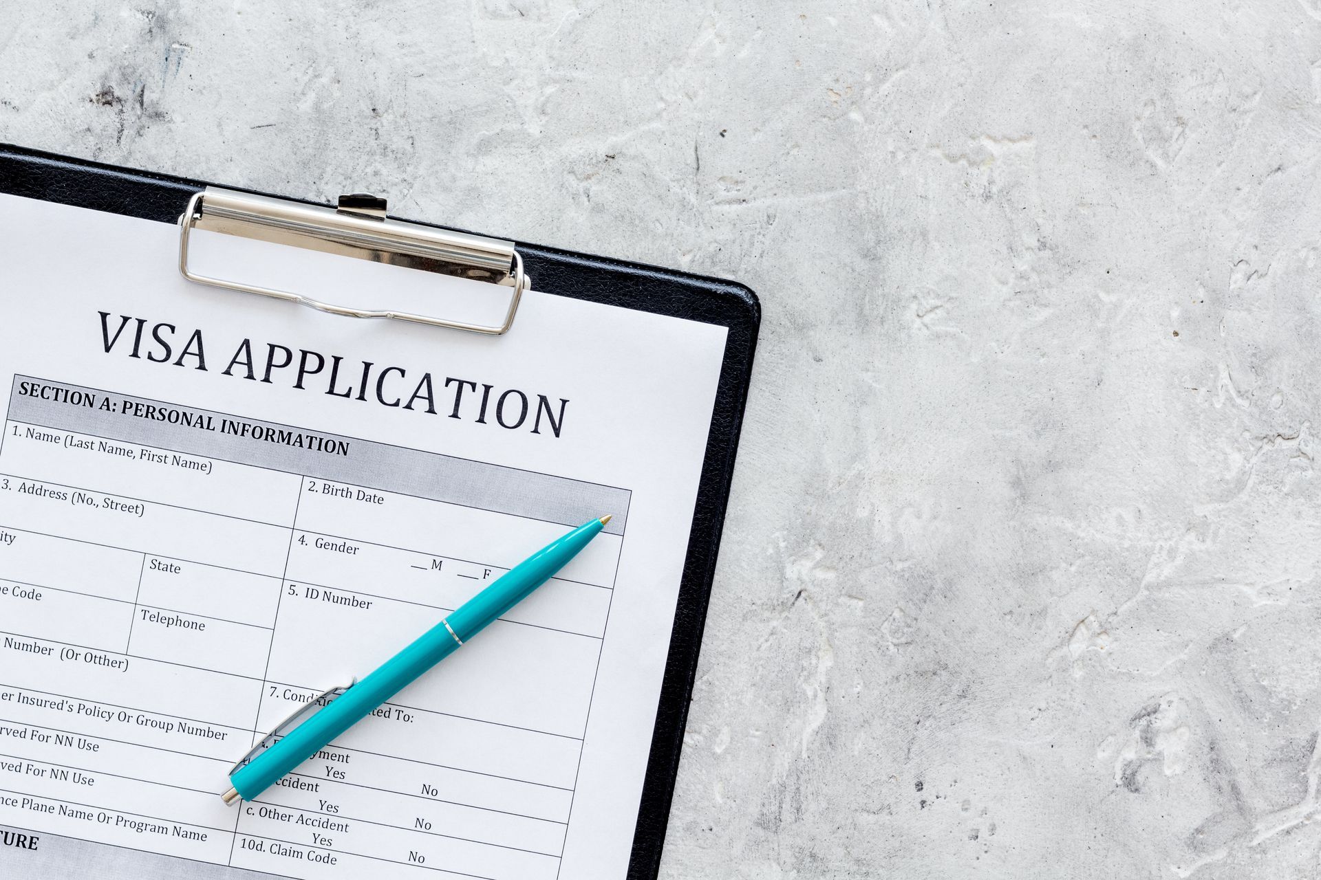 Clipboard with visa application form and blue pen on a gray surface.