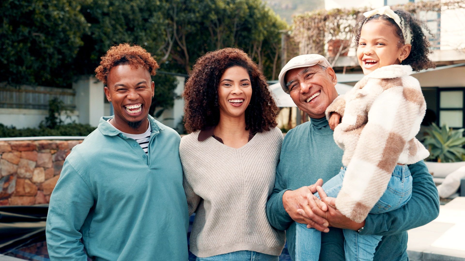 A family poses outdoors, smiling and laughing together with a man holding a child in his arms.