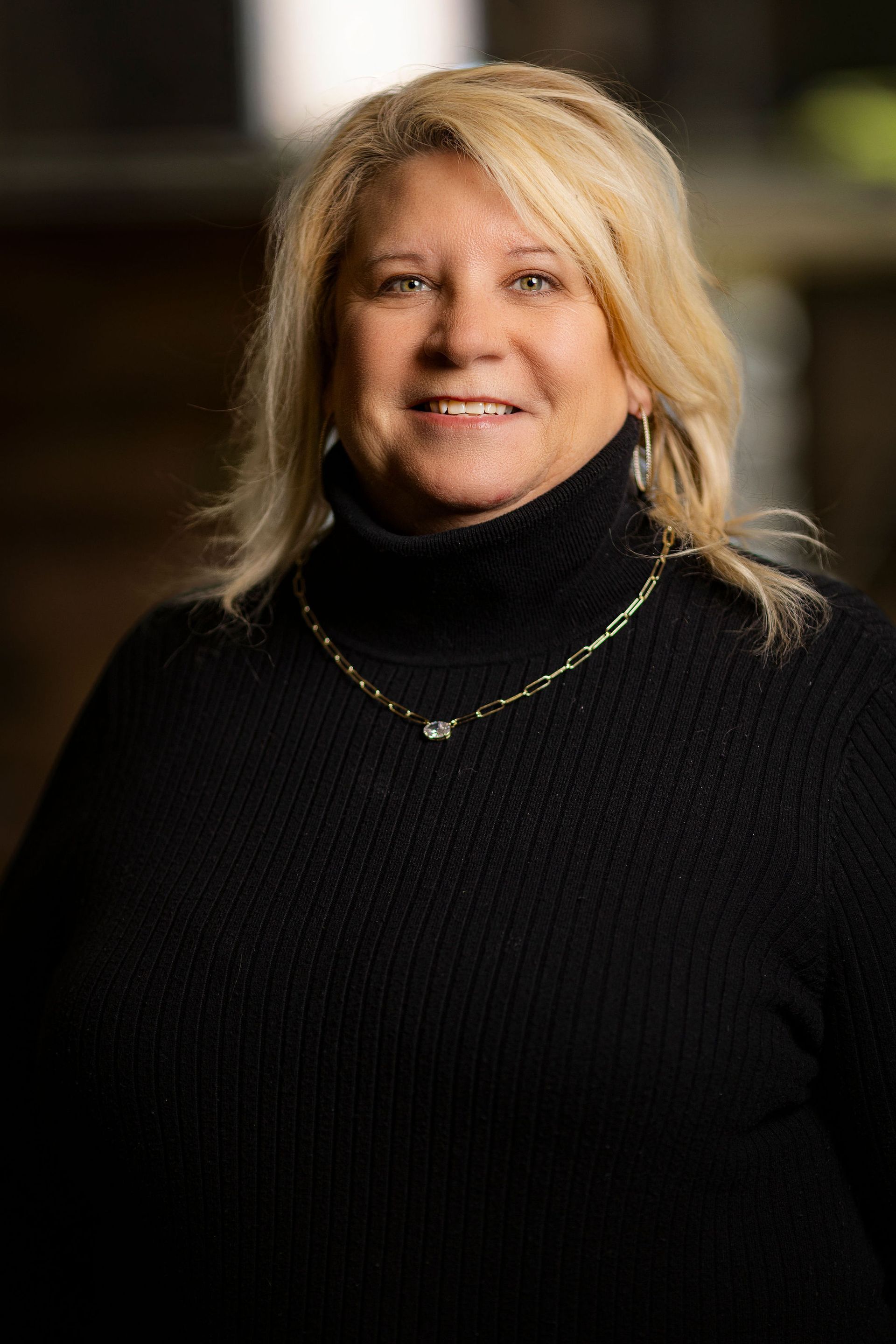 A woman wearing a black jacket and a polka dot shirt is smiling.