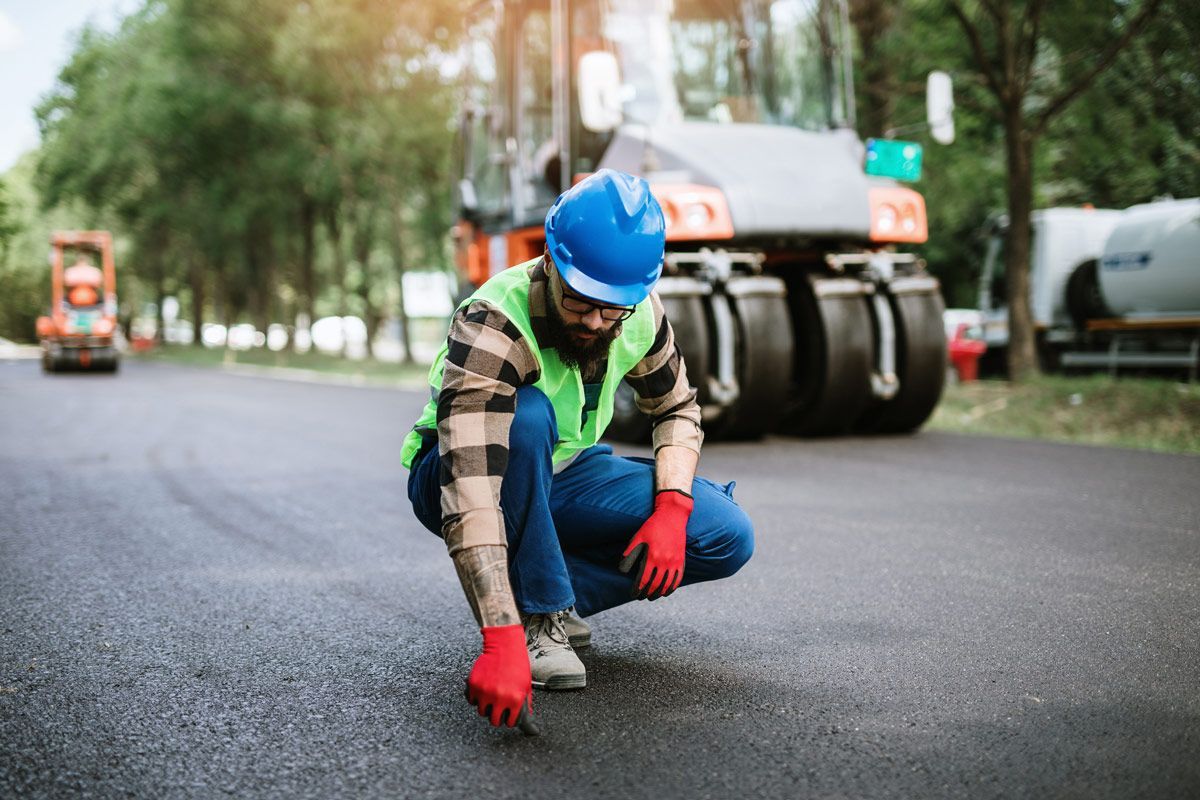 A Construction Worker Is Kneeling on The Road — Omaha, NE — Omaha Paving Company