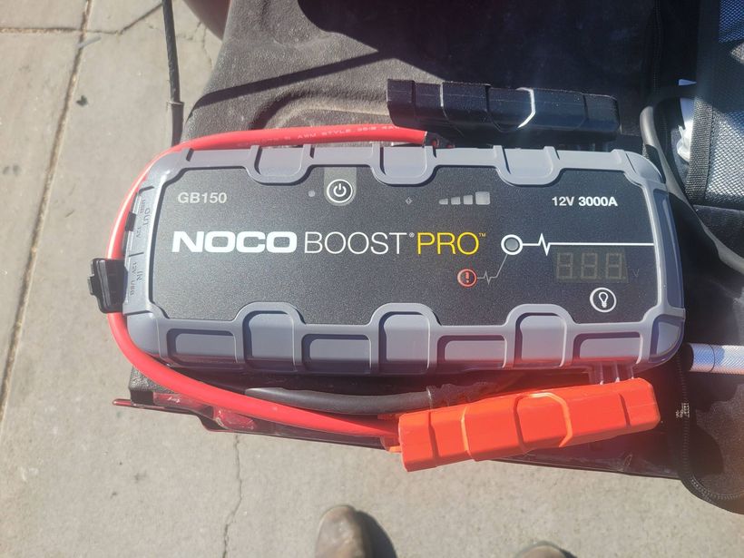 NOCO Boost Pro jump starter in a red and black carrying case on a sidewalk