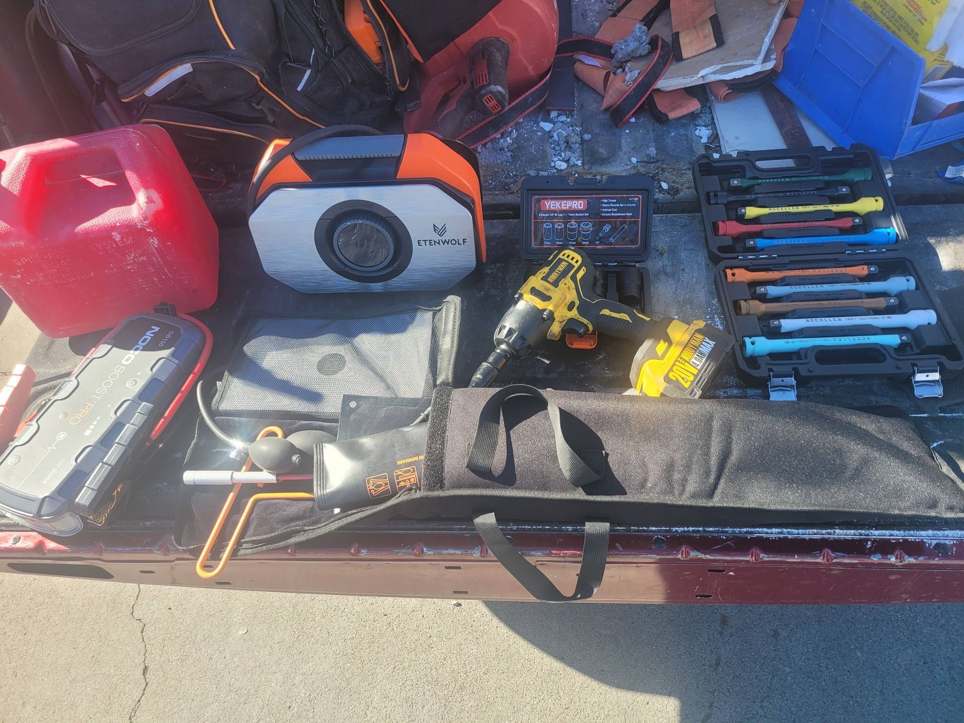 Tool kit with drill, hand tools, batteries, and red fuel can in a vehicle trunk.