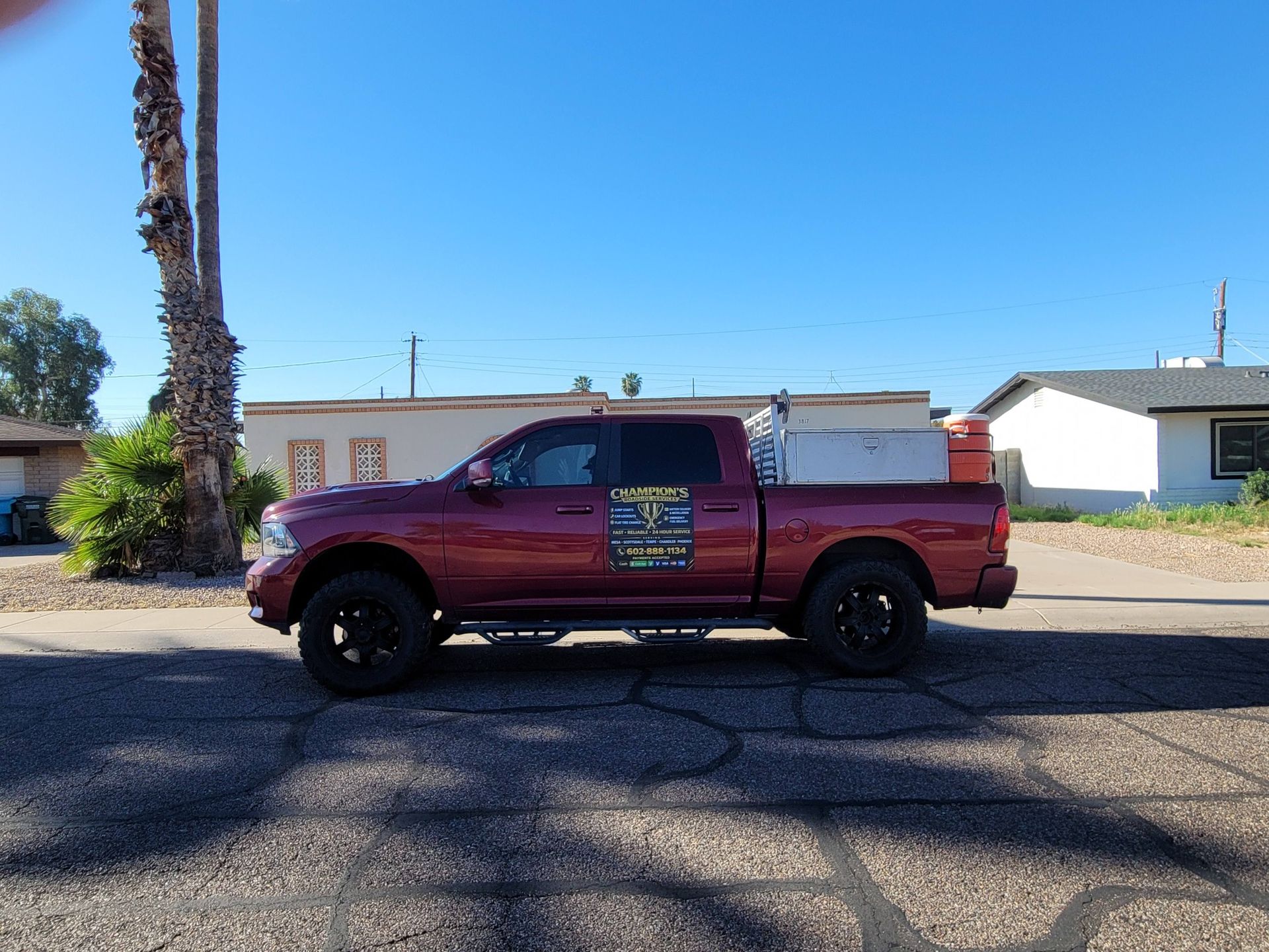 Maroon pickup truck parked on a sunny street with houses and a tall palm tree in the background