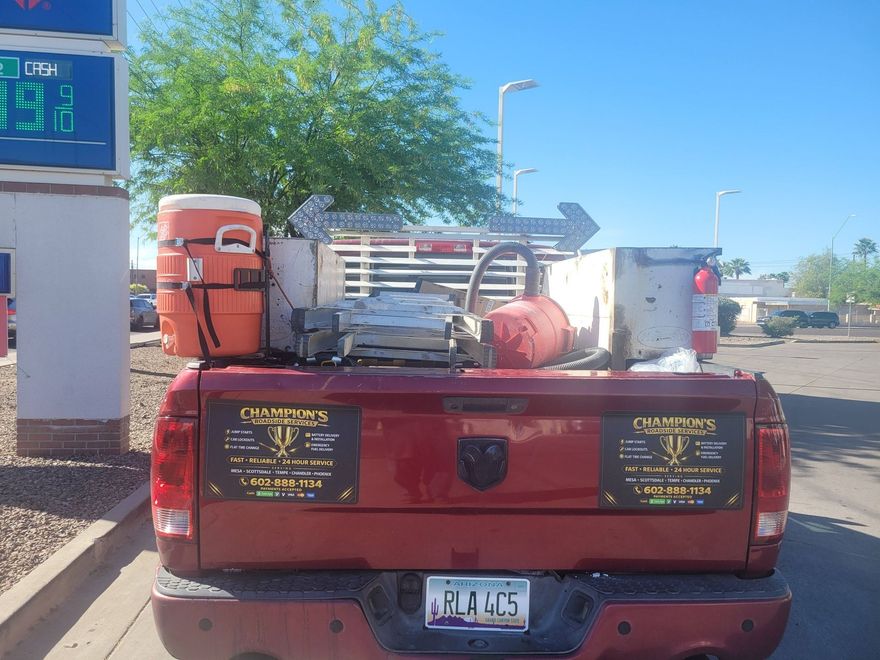 Red pickup truck with tools and equipment in the bed, parked at a gas station on a sunny day
