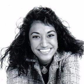 A woman with long curly hair is smiling in a black and white photo.