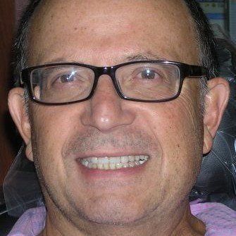 A man wearing glasses and a pink shirt is smiling.