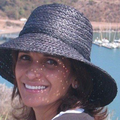 A woman wearing a black hat is smiling in front of a body of water