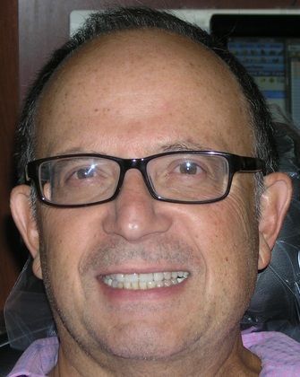 A man wearing glasses and a pink shirt is smiling.