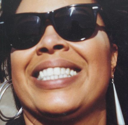 A woman wearing sunglasses and hoop earrings is smiling