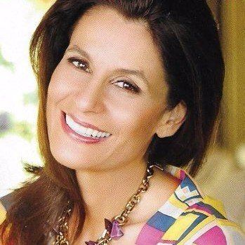 A woman wearing a necklace and a colorful shirt smiles for the camera