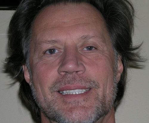 A man with long hair and a beard smiles for the camera