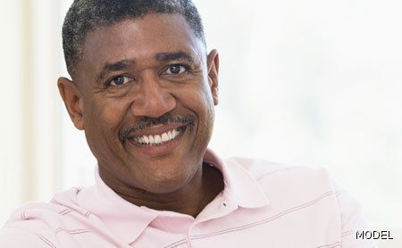 A man in a pink shirt is smiling and looking at the camera.