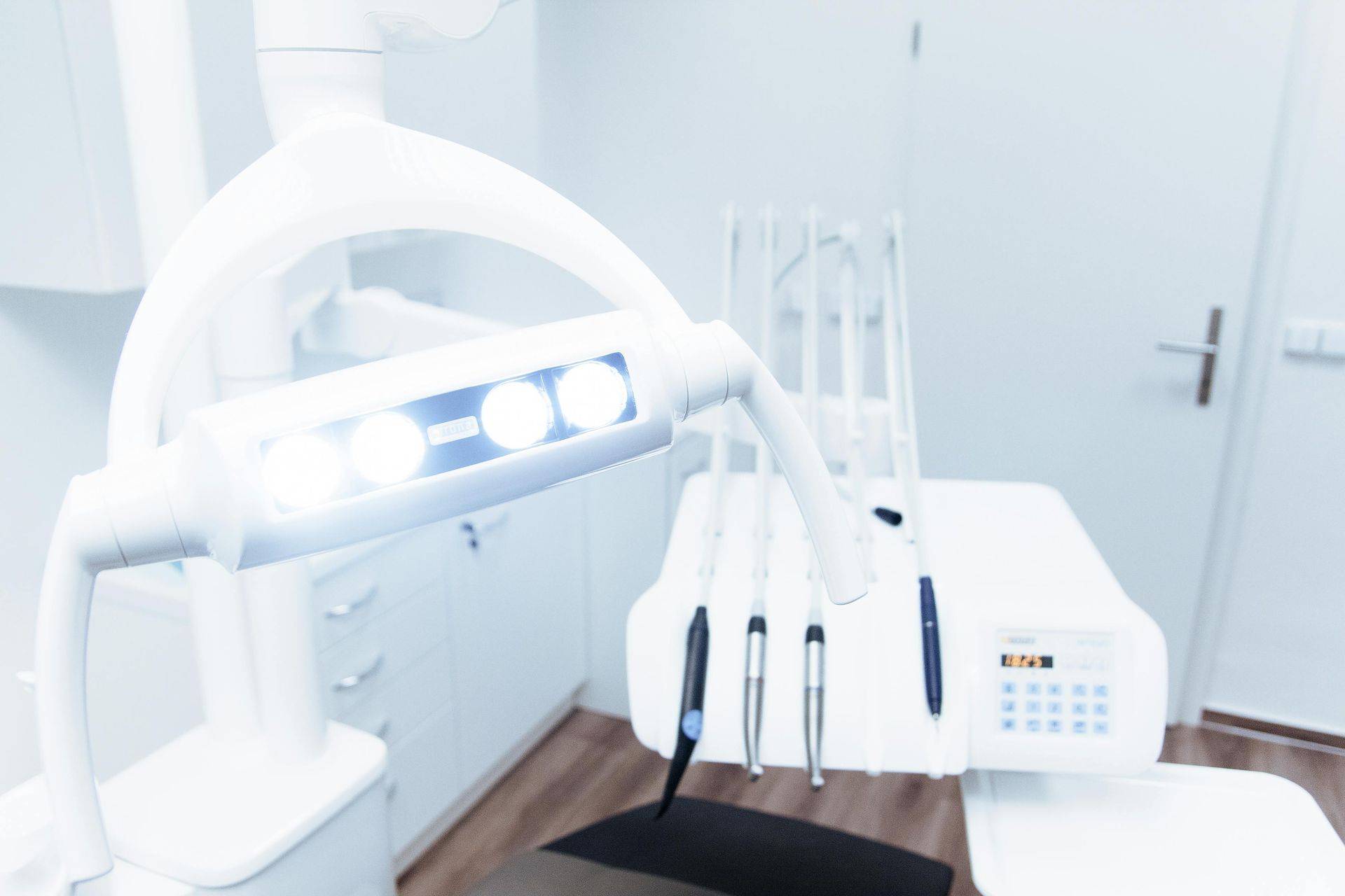 Dental office, focus on bright overhead light and dental tools in a white room.