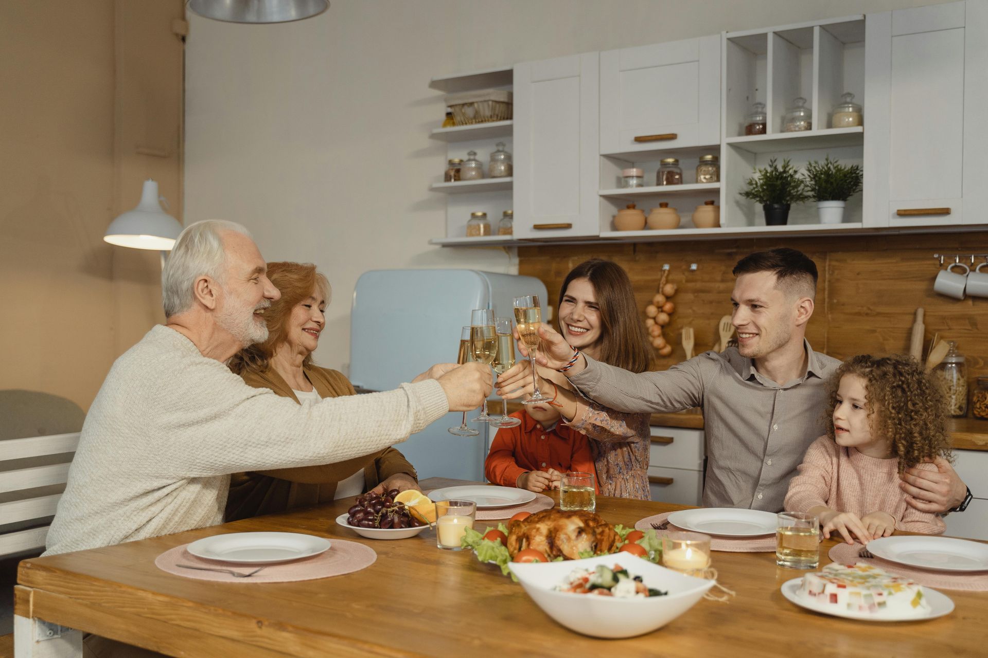 Family cheers with champagne at a wooden table in a kitchen.