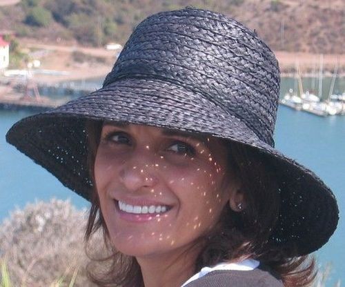 A woman wearing a black hat is smiling in front of a body of water