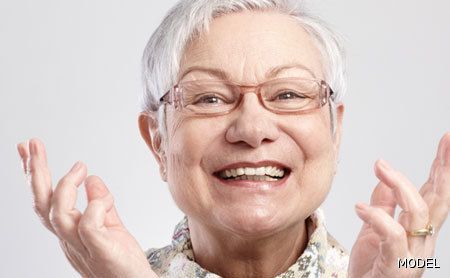 An elderly woman wearing glasses is smiling with her hands in the air.