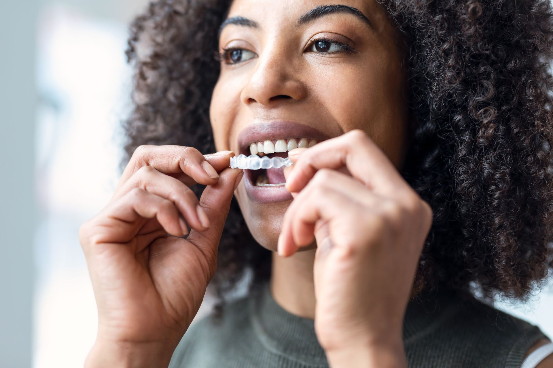 Woman with curly hair putting in clear aligners.