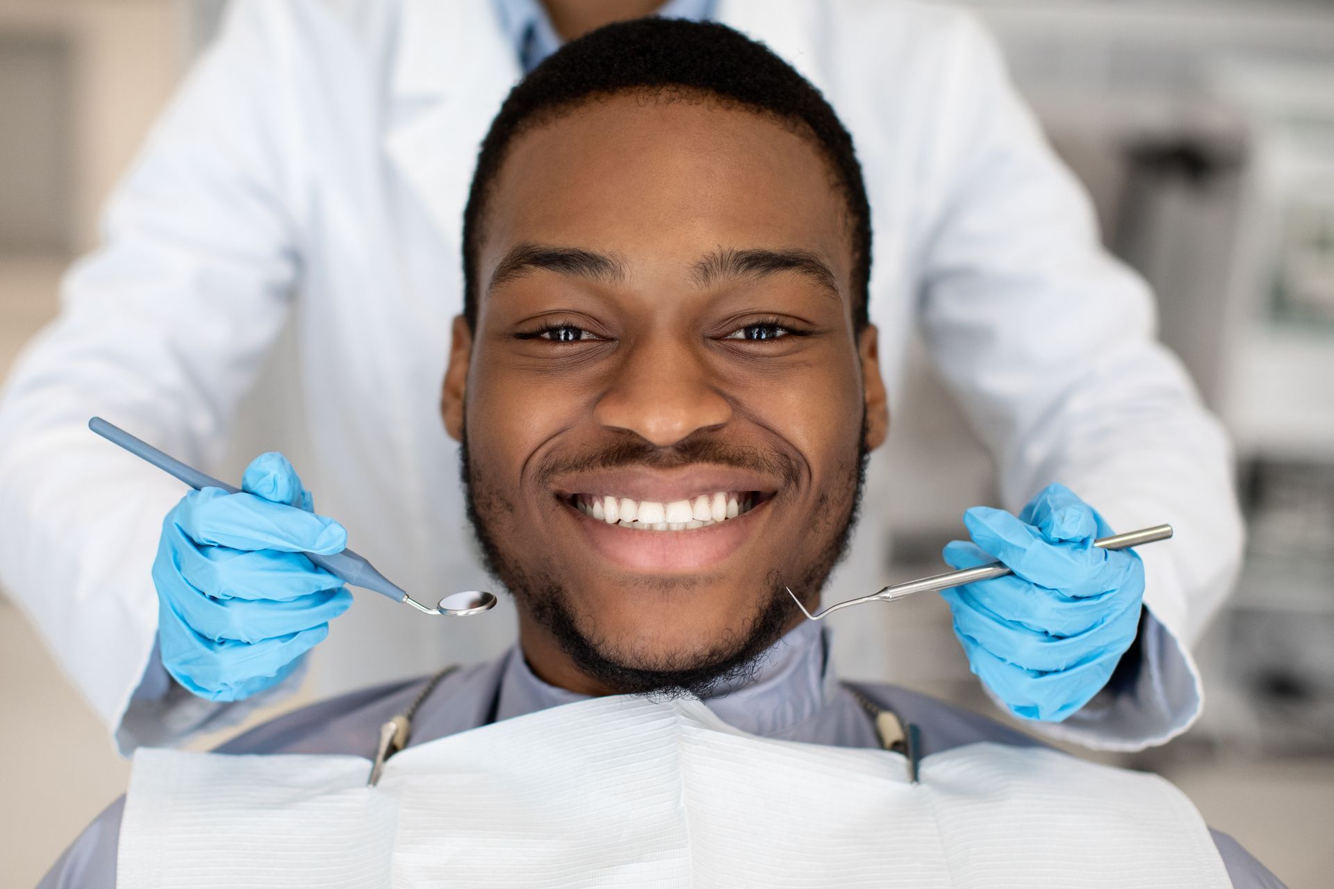 Man smiling at the dentist. A dentist holds tools with blue gloves in a dental office.