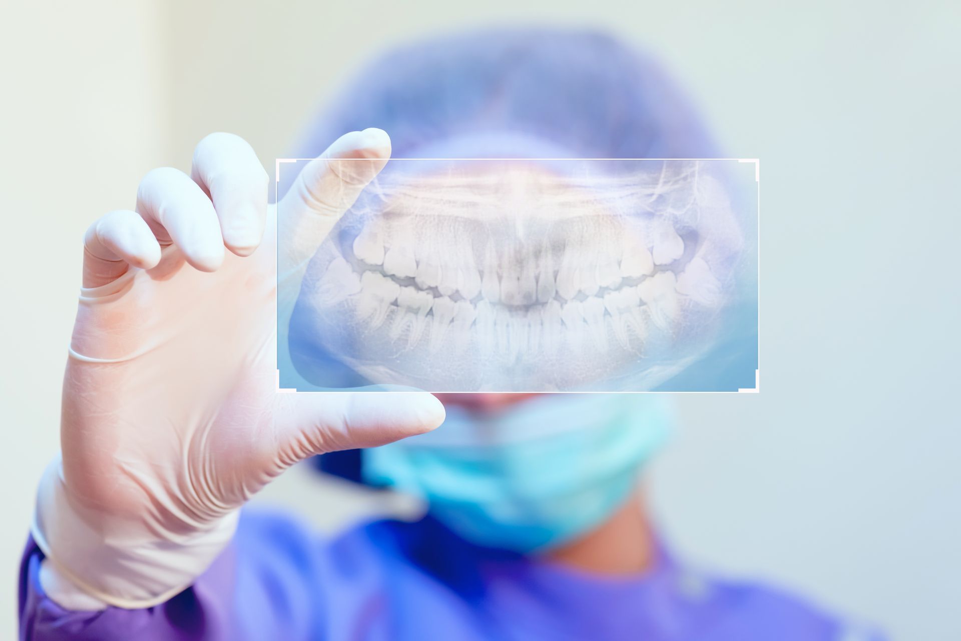 Dentist holding up a panoramic dental x-ray. Shows teeth; wears gloves, mask, and cap; in a medical setting.