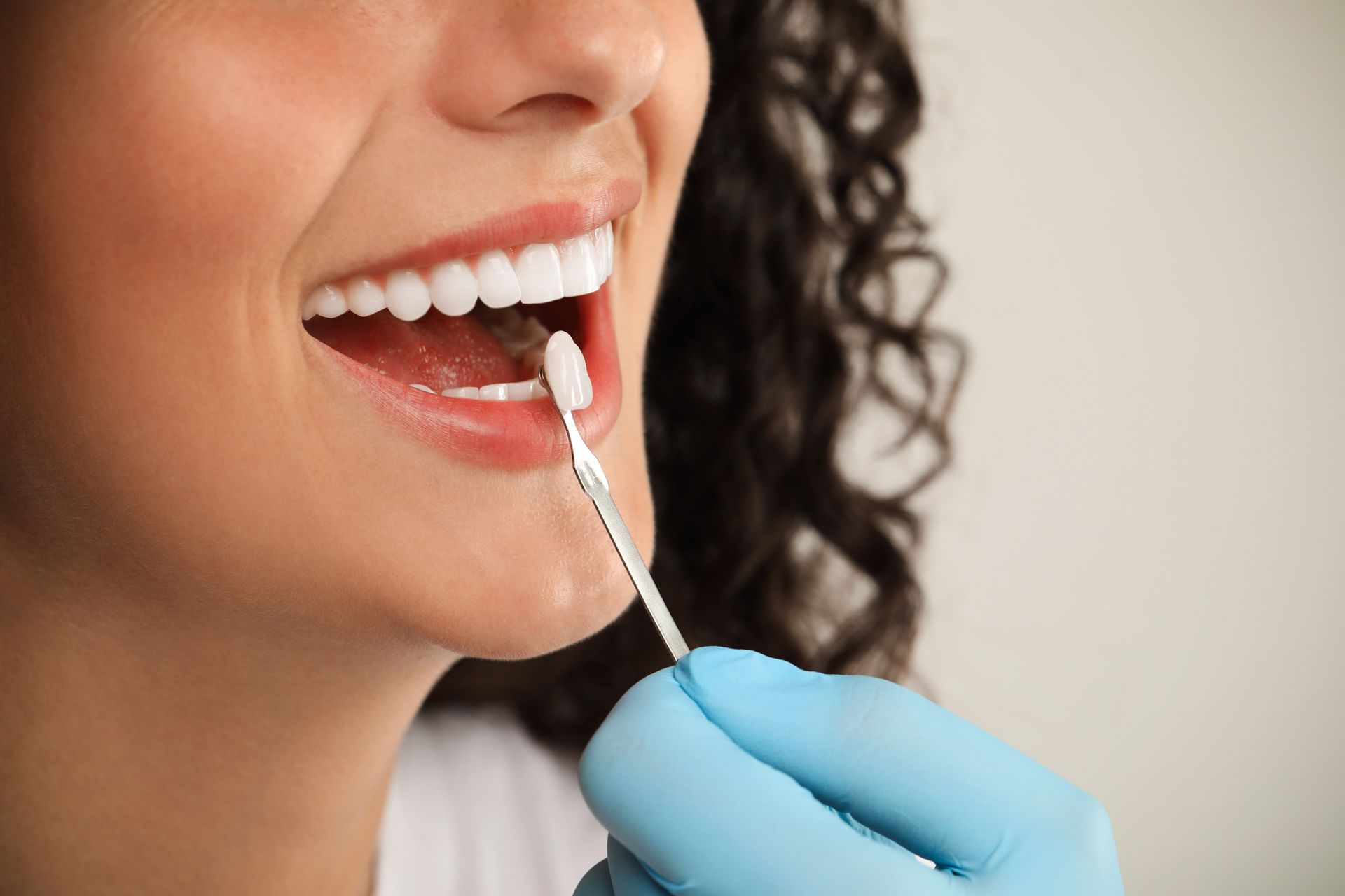 Woman smiling, dental work in progress, doctor in blue glove holding dental tool.