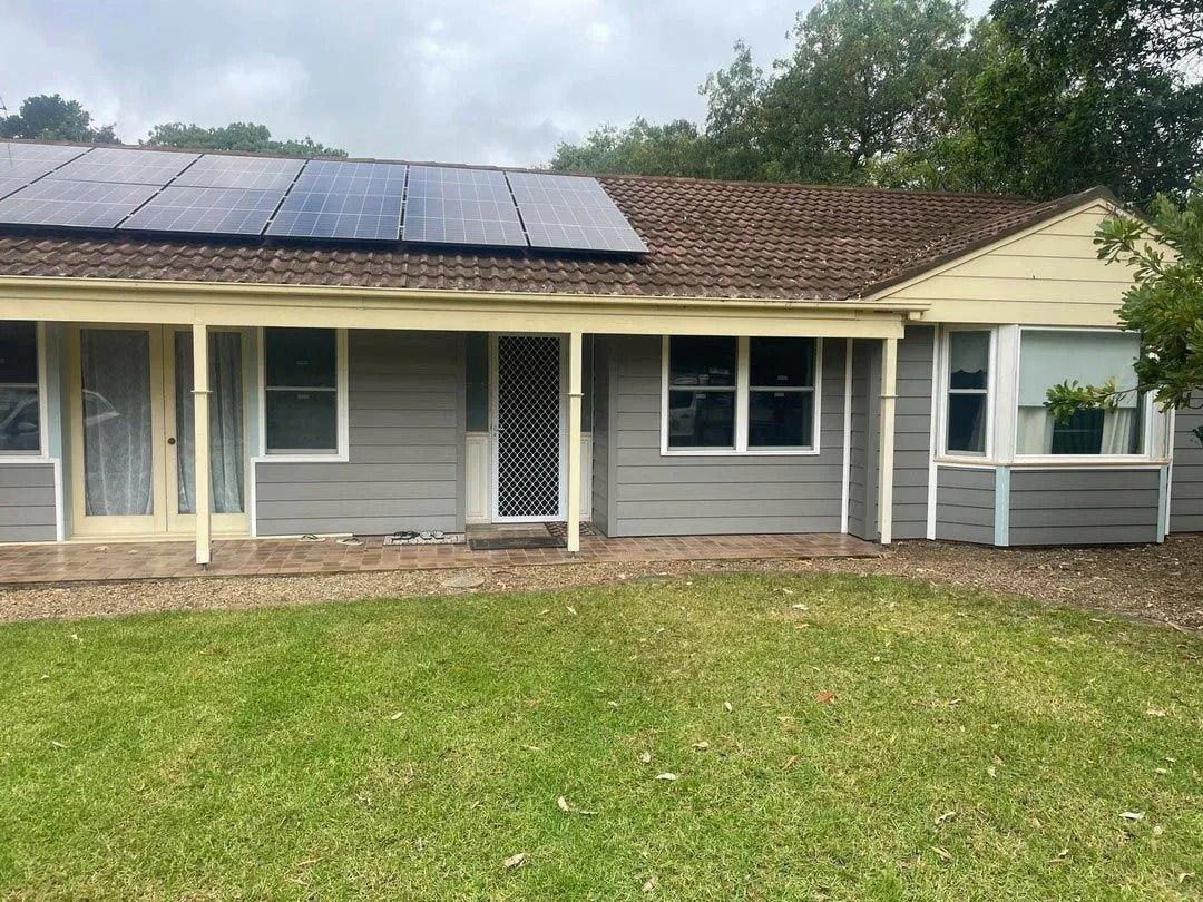 A gray house with a solar panel roof, a porch, and a green lawn. Overcast day.