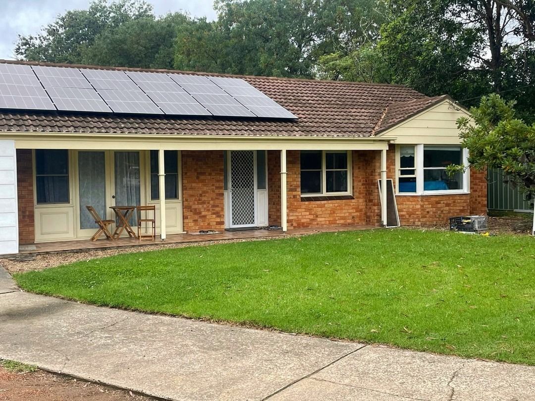 A one-story brick house with a lawn and solar panels on the roof. A concrete path leads to the house.
