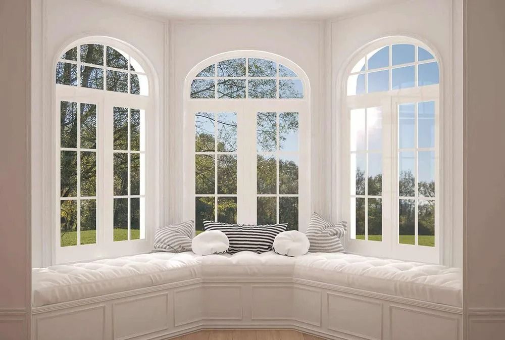 Bay window with three arched windows, a cushioned window seat, and pillows. Outside, trees and blue sky are visible.