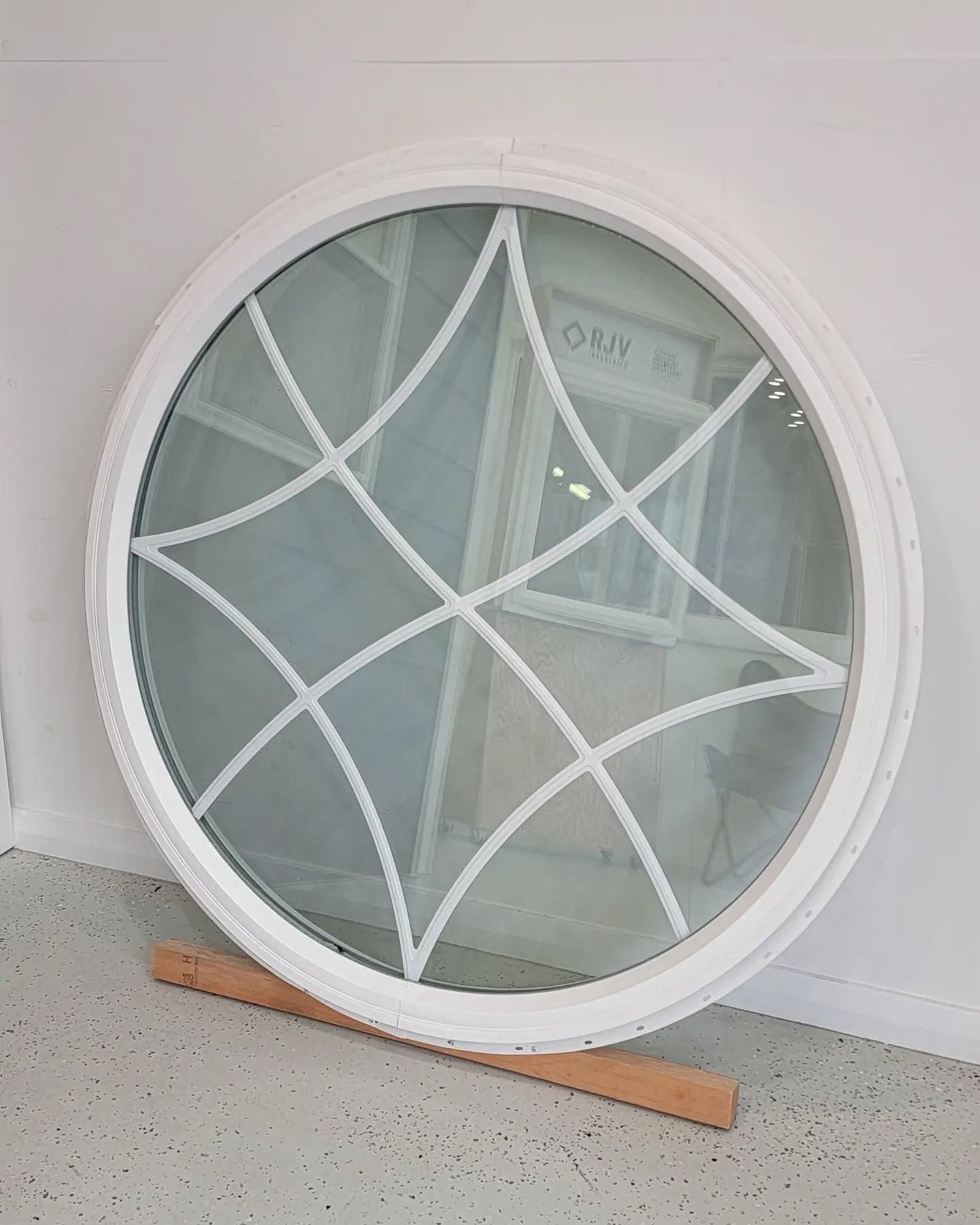 White, circular window with geometric grid design, resting on a wooden support against a white wall.