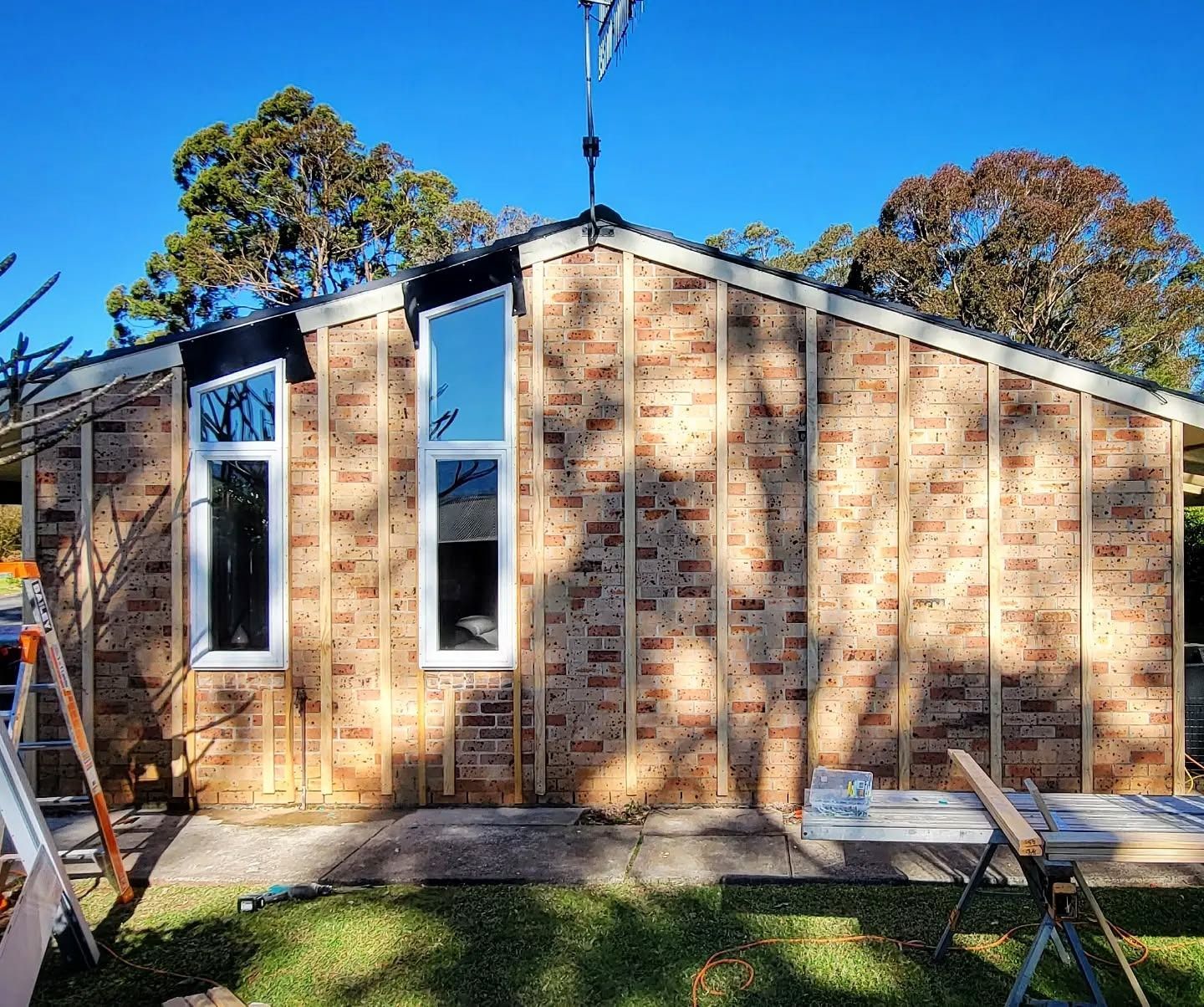 Brick building exterior under construction; window frames installed. Wooden beams and a blue sky background.