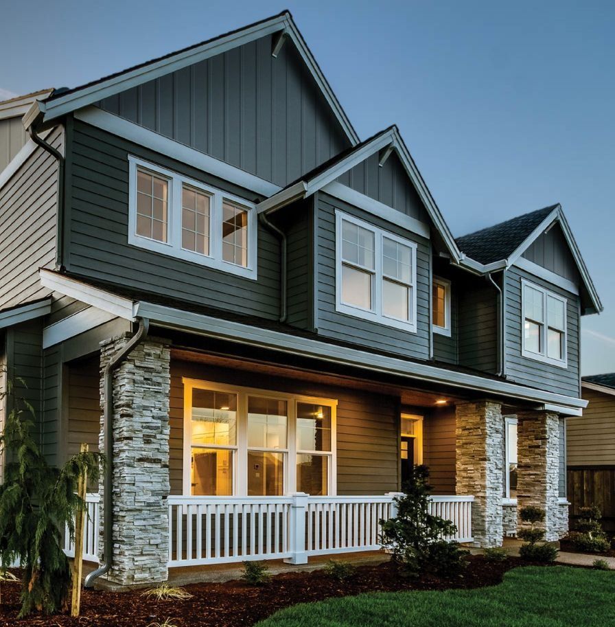 Two-story house with gray siding, stone accents, white trim, and a small front porch, set against a clear blue sky.
