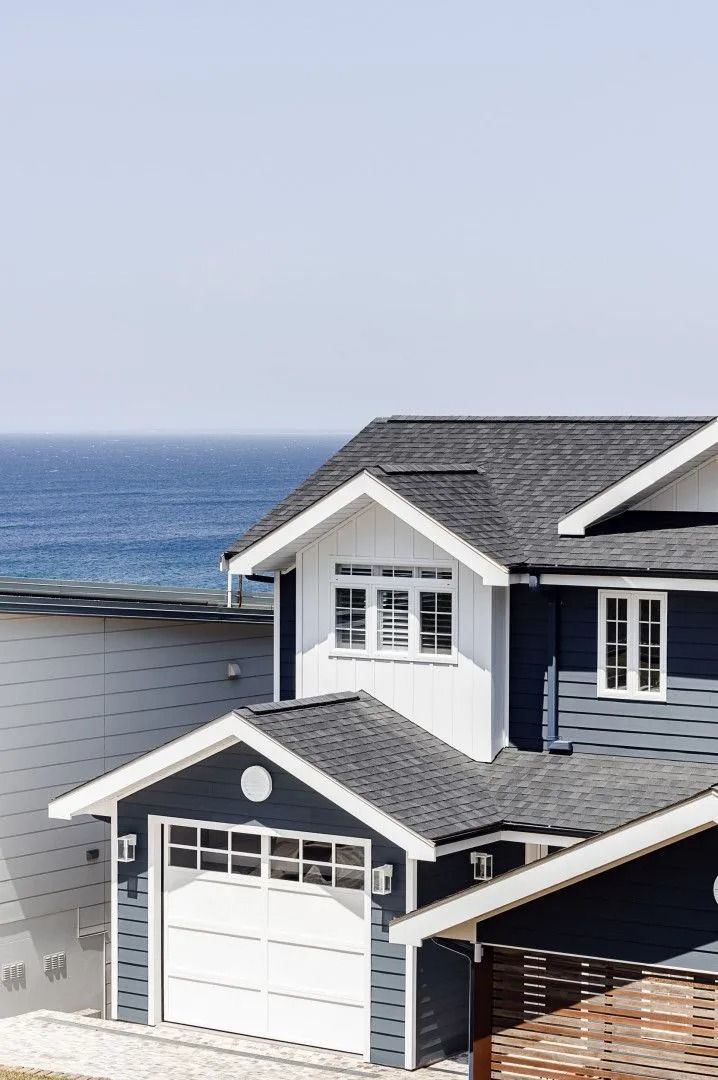 Blue and white house with a gray roof, overlooking the ocean on a sunny day.