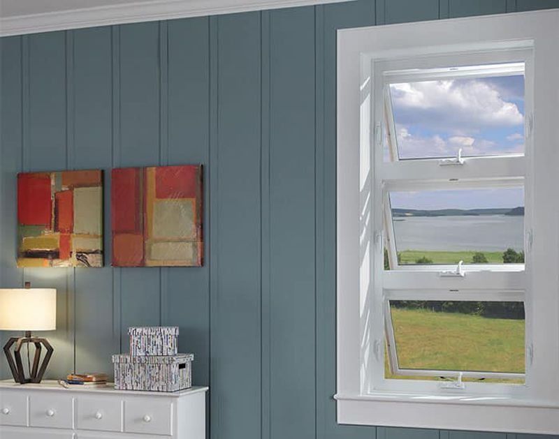 Open double-hung window in a room with blue paneled walls, overlooking a landscape with a lake and sky.