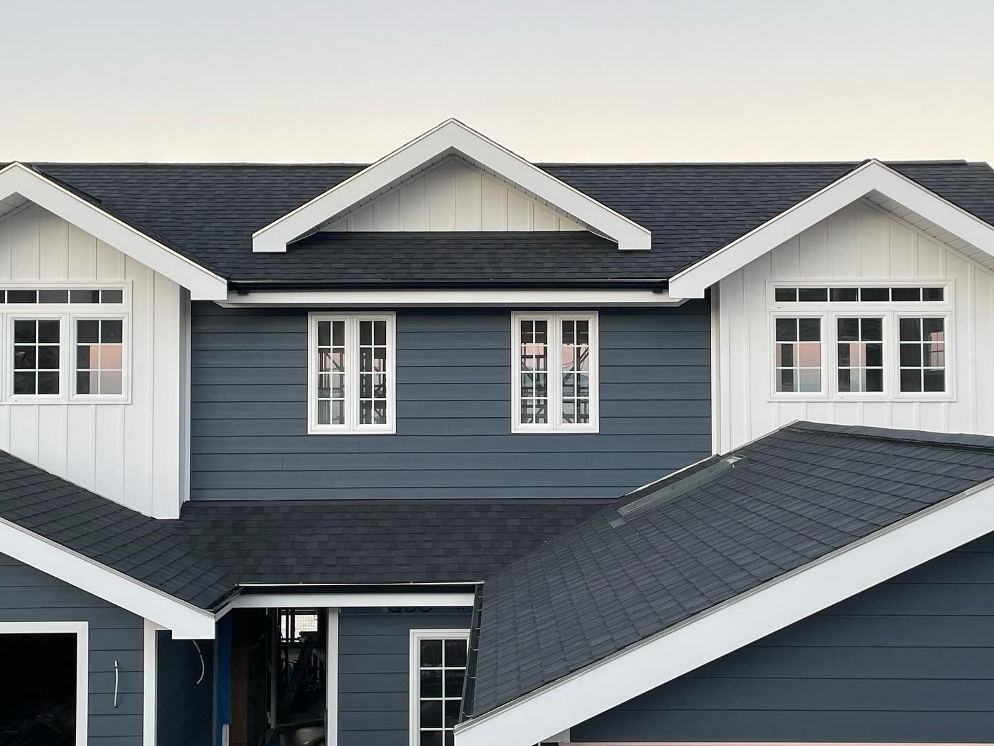 Two-story house with dark gray siding, white trim, and a dark gray roof. Features multiple white-framed windows.