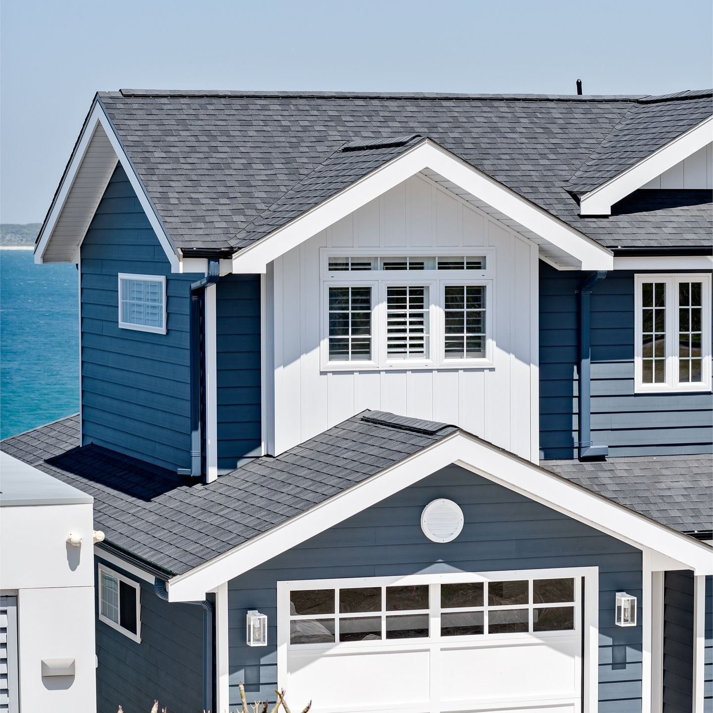Blue and white coastal house with dark gray roof against a blue ocean backdrop.