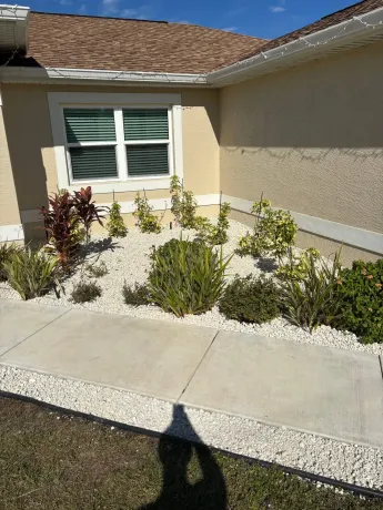 A house exterior with a garden bed filled with plants and white pebbles next to a sidewalk.